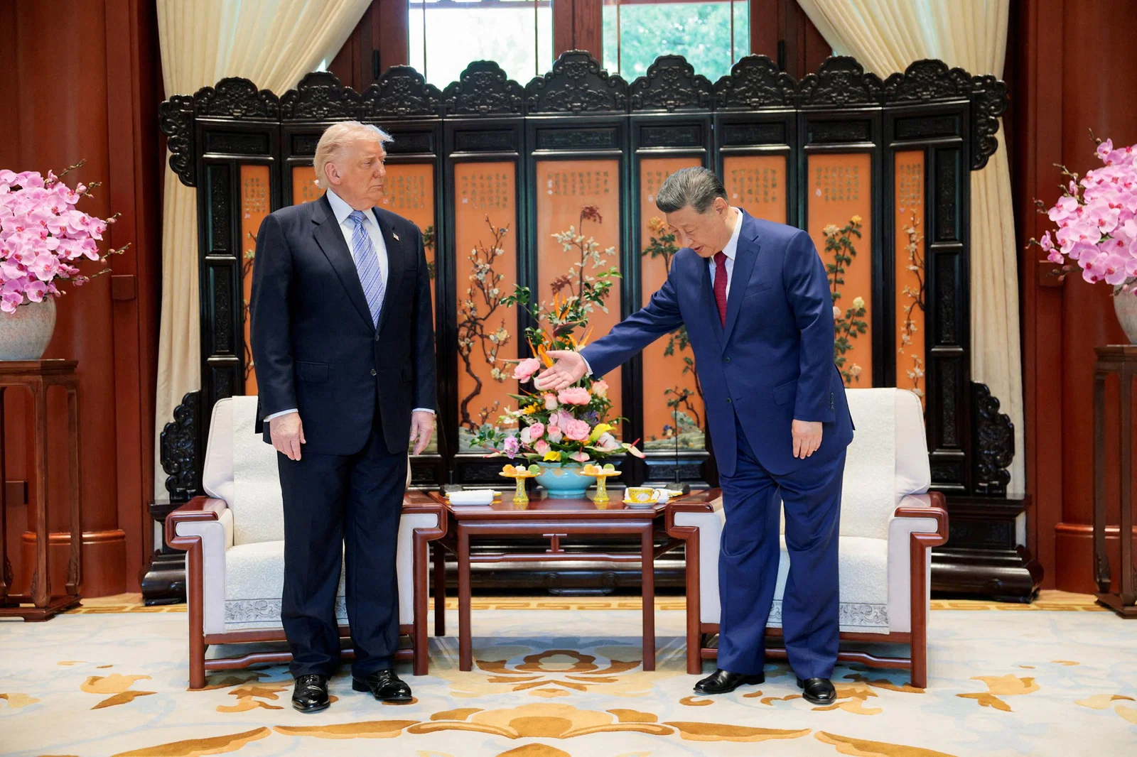 Two men in suits prepare to sit down in an ornate room