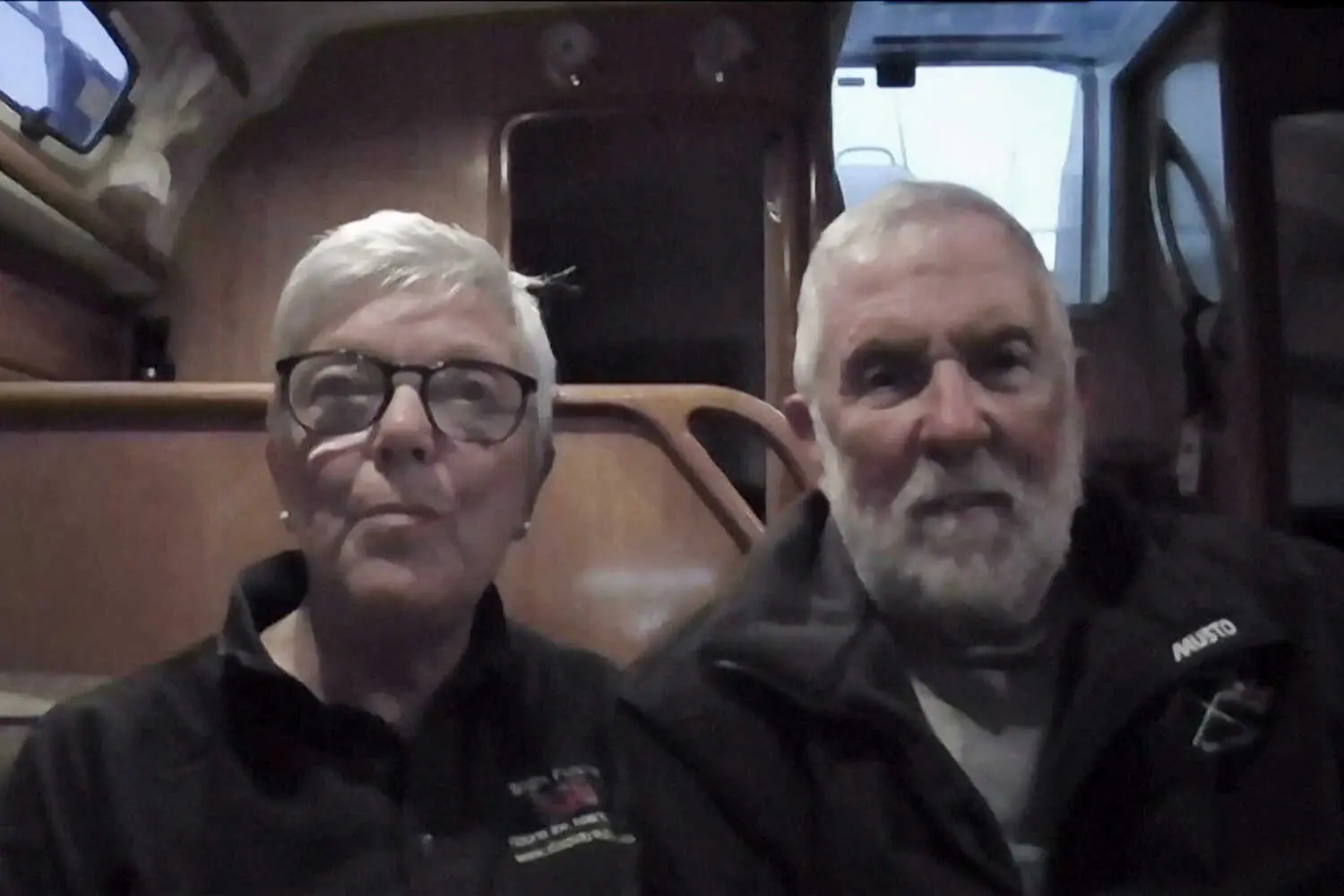 A woman and a man sit together inside a boat with wooden interiors.
