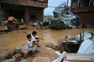 Children sit next to damaged houses in Liulan village