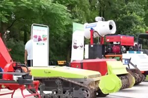 Row of red and green forestry machines including a rubber-tracked crawler and a mounted white mist blower under trees at an outdoor equipment exhibition in China.