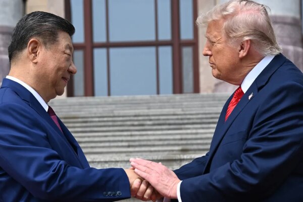 Xi Jinping and Donald Trump shake hands while looking at each other in front of stone steps.