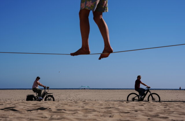 Two people ride bicycles along a beach path as a man balances on a slackline in Santa Monica, Calif., Wednesday, July 8, 2026. (AP Photo/Jae C. Hong)