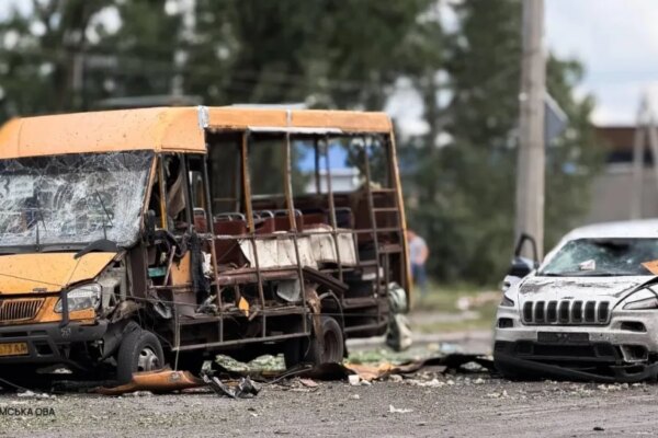 A heavily damaged yellow bus and a damaged white car sit on a debris-strewn road.