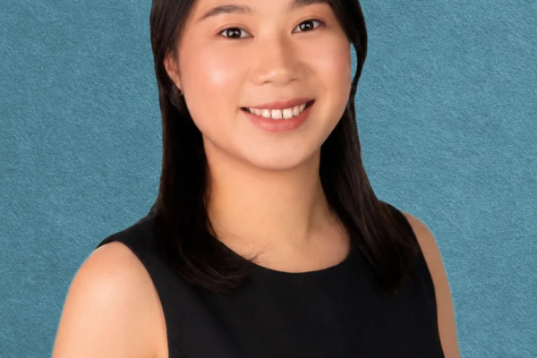 Smiling person with long hair in a black top, blue textured background.
