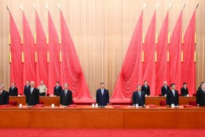 Senior Chinese government officials in dark suits standing at podium before large red ceremonial flags at formal state event