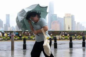 A woman struggles with her umbrella in strong wind and rain ahead of Typhoon Dolphin at Huangpu District of Shanghai on Sunday, 9 August 2026.