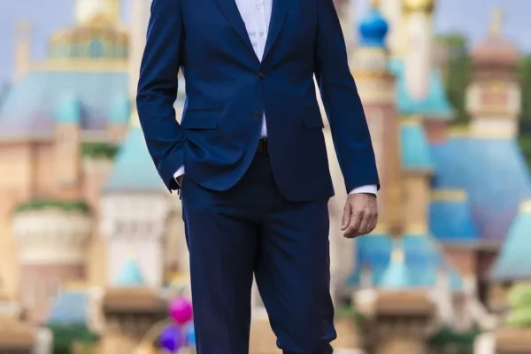 Man in a blue suit, Tim Sypko, walking in front of a colourful Disney castle at Hong Kong Disneyland