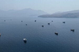 Drone view of multiple vessels in the Strait of Hormuz, with mountains in the background.