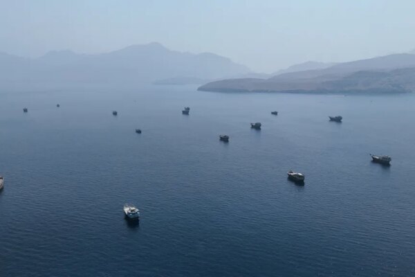 Drone view of multiple vessels in the Strait of Hormuz, with mountains in the background.
