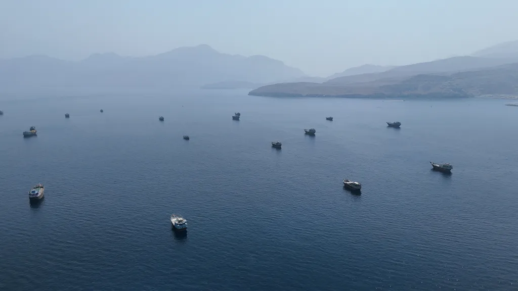 Drone view of multiple vessels in the Strait of Hormuz, with mountains in the background.